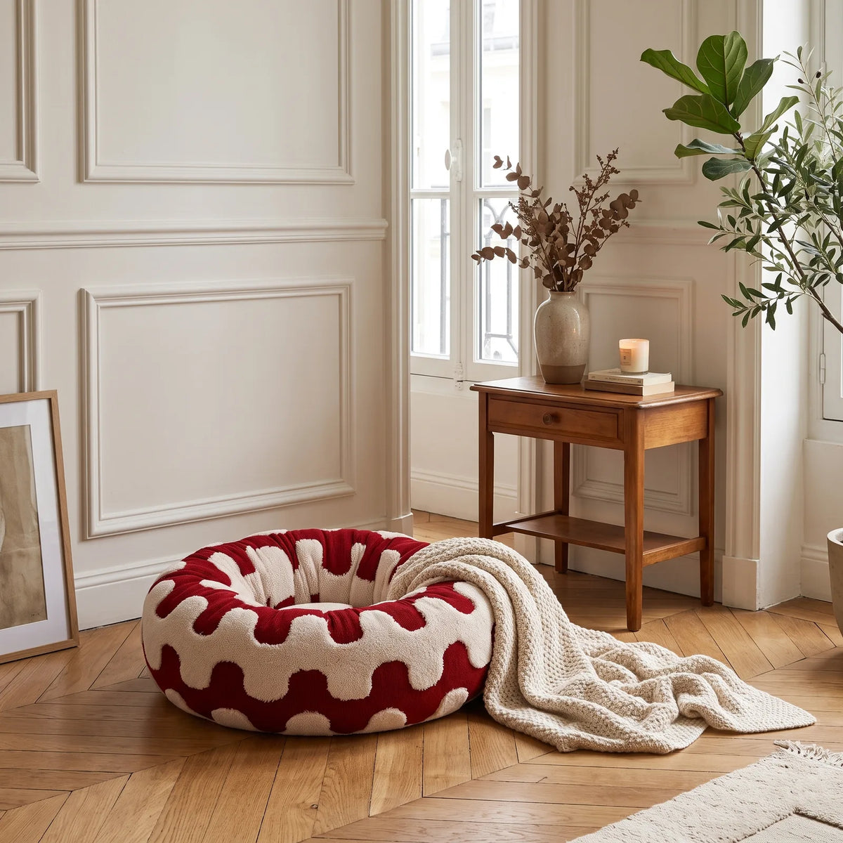 Panier rond anti-stress rouge à motif vagues installé dans un coin déco avec plaid et plante